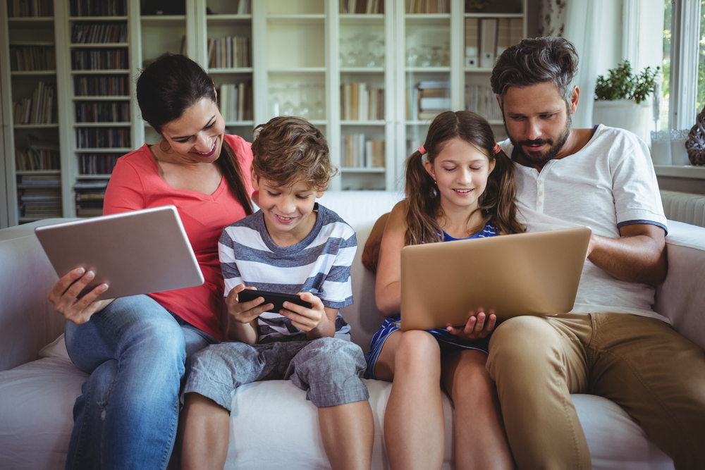 Happy family sitting on sofa and using laptop, mobile phone and digital tablet at home Happy family sitting on sofa and using laptop, mobile phone and digital tablet at home